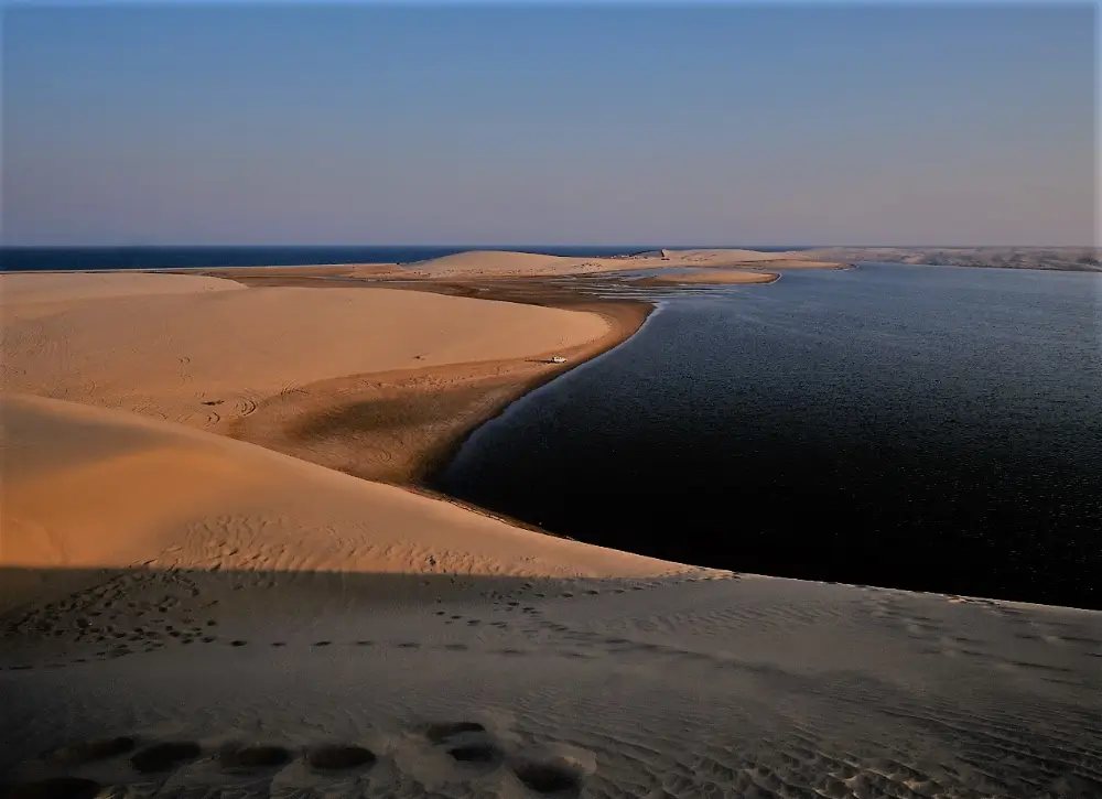 A sandy beach with water and sand dunes.