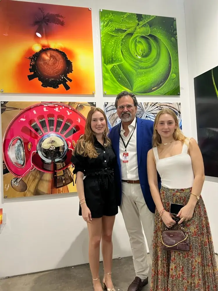 Two women and a man standing in front of some paintings.