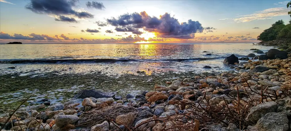 A sunset over the ocean with rocks in the foreground.