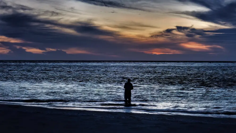 A person standing in the water at sunset.